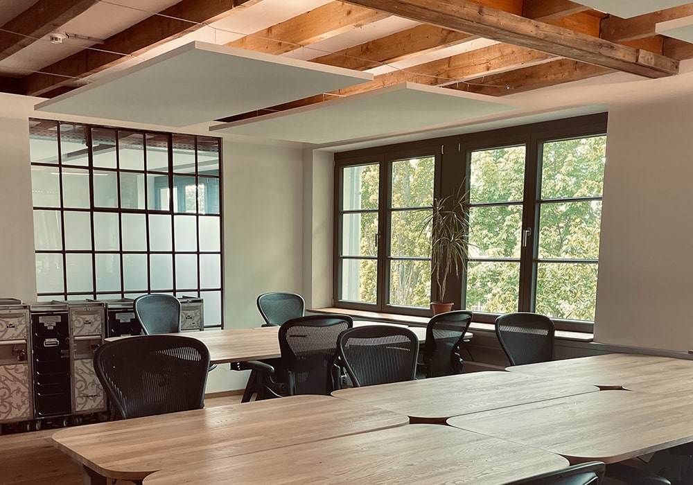 "Heller und einladender Coworking-Bereich mit einem langen Holztisch, Stühlen und großen Fenstern, die viel Tageslicht im Denkwerk Herford hereinlassen
