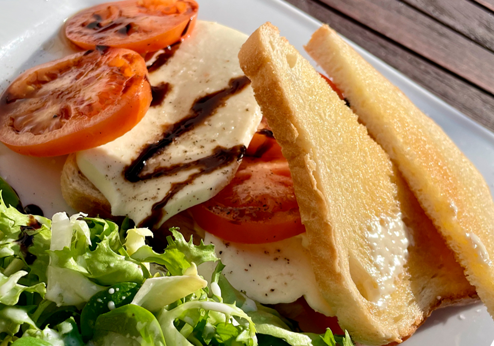 Frisch zubereitetes Frühstück mit Mozzarella, Tomaten, Balsamico und Salat auf einem weißen Teller.