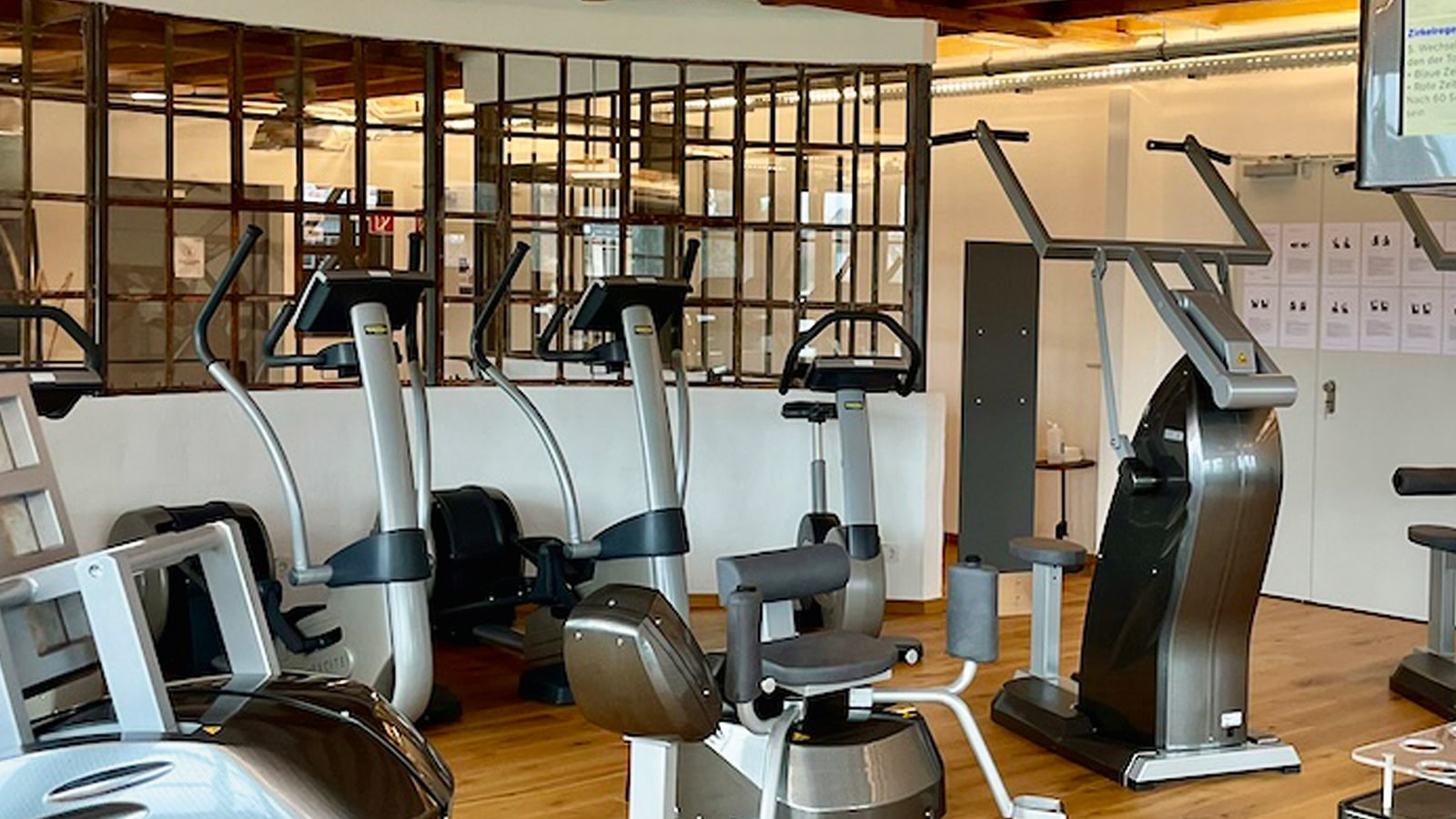Fitnessstudio-Ausrüstung in einem Raum mit Holzboden und dekorativer Glaswand.