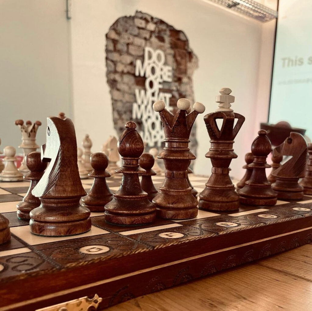 Nahaufnahme eines Schachspiels mit hölzernen Figuren, Hintergrundkunstwerk mit der Aufschrift 'DO MORE OF WHAT MAKES YOU HAPPY' im 'Denkwerk Herford'.