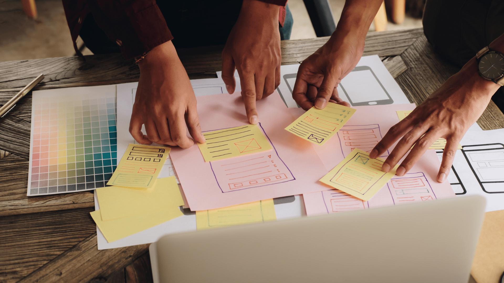 Zwei Personen planen die Struktur einer Website mit Hilfe von Farbpaletten und skizzierten Vorlagen auf Papier.