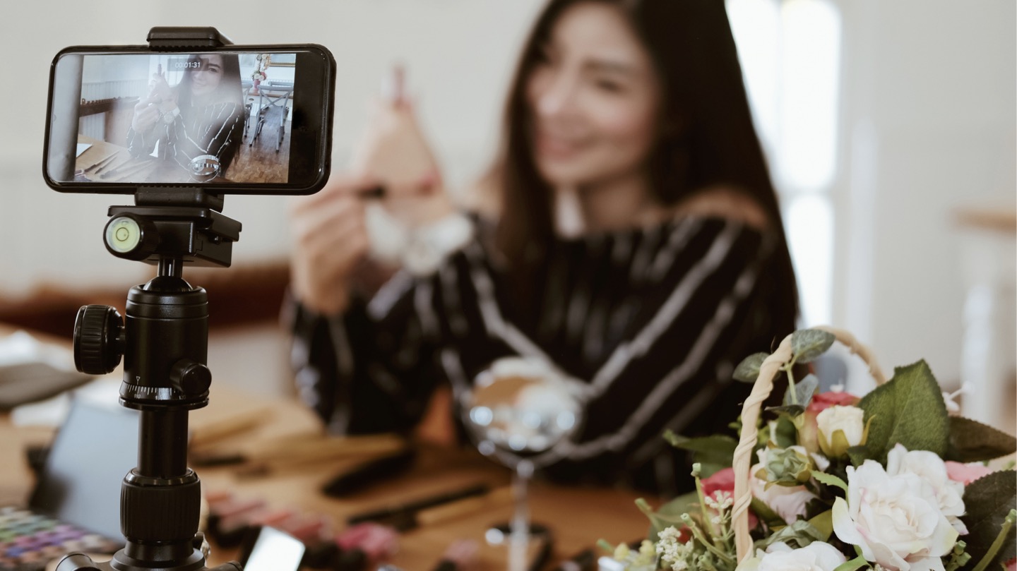 Eine lächelnde Bloggerin nimmt ein Video mit ihrem Smartphone auf, das auf einem Stativ montiert ist, was die Bedeutung der Impressumspflicht für Blogger und Influencer unterstreicht