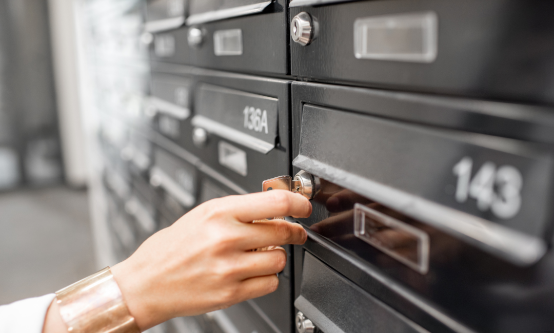 Eine Person öffnet eine schwarze Postbox mit der Nummerierung 143 in einer Reihe von identischen Postfächern.