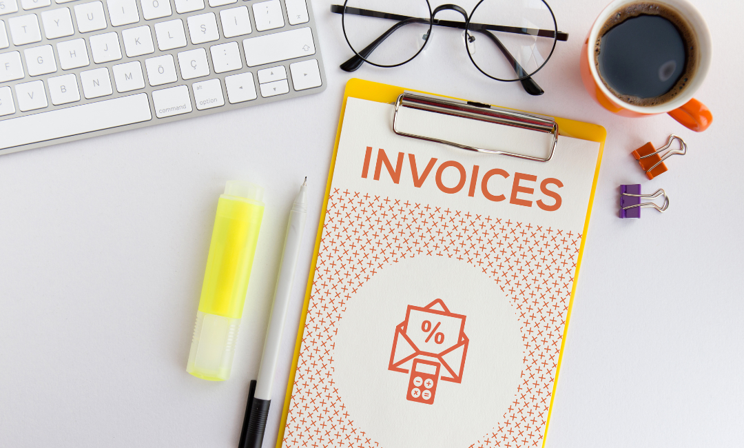 Arbeitsplatz mit Tastatur, Brille, Kaffee und einem Clipboard mit der Aufschrift "INVOICES", was die Bedeutung eines Steuerberaters für die Buchhaltung betont.