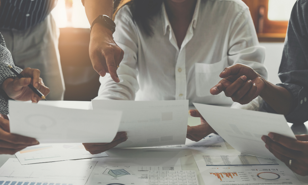 Ein Steuerberaterteam überprüft und diskutiert Finanzberichte, wobei ein Steuerberater auf einen relevanten Aspekt in einem Dokument hinweist.