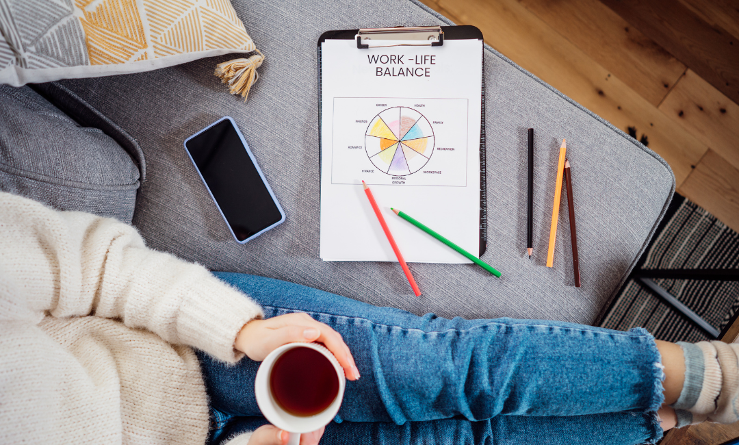 Eine Person betrachtet entspannt ein Diagramm zur Work-Life-Balance, das auf einem Clipboard liegt, neben einem Smartphone und farbigen Stiften auf einem gemütlichen Sofa.
