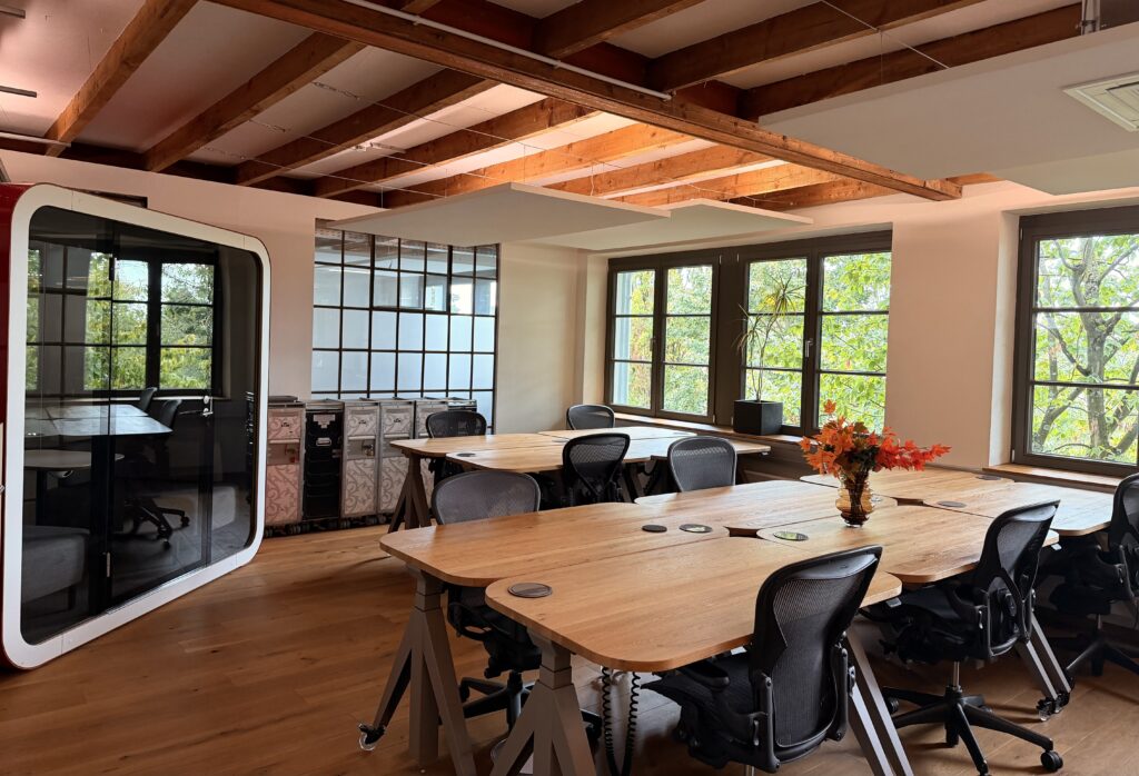 Modernes Coworking-Space mit großen Fenstern, Holzschreibtischen, ergonomischen Bürostühlen und schallgedämmter Telefon-/Meetingbox