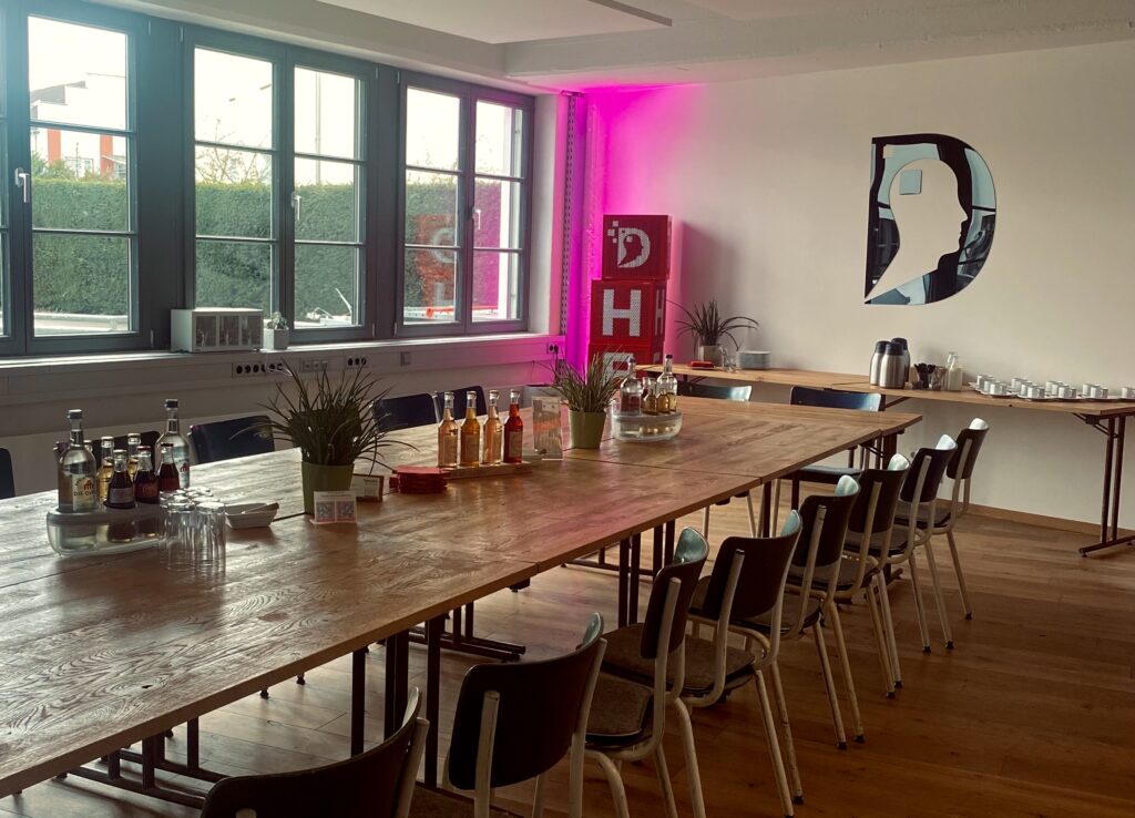 Besprechungsraum Brainforce Three im Denkwerk Herford mit großem Holztisch, Getränken, Pflanzen und stilvoller Beleuchtung – ideal für Meetings und Workshops.