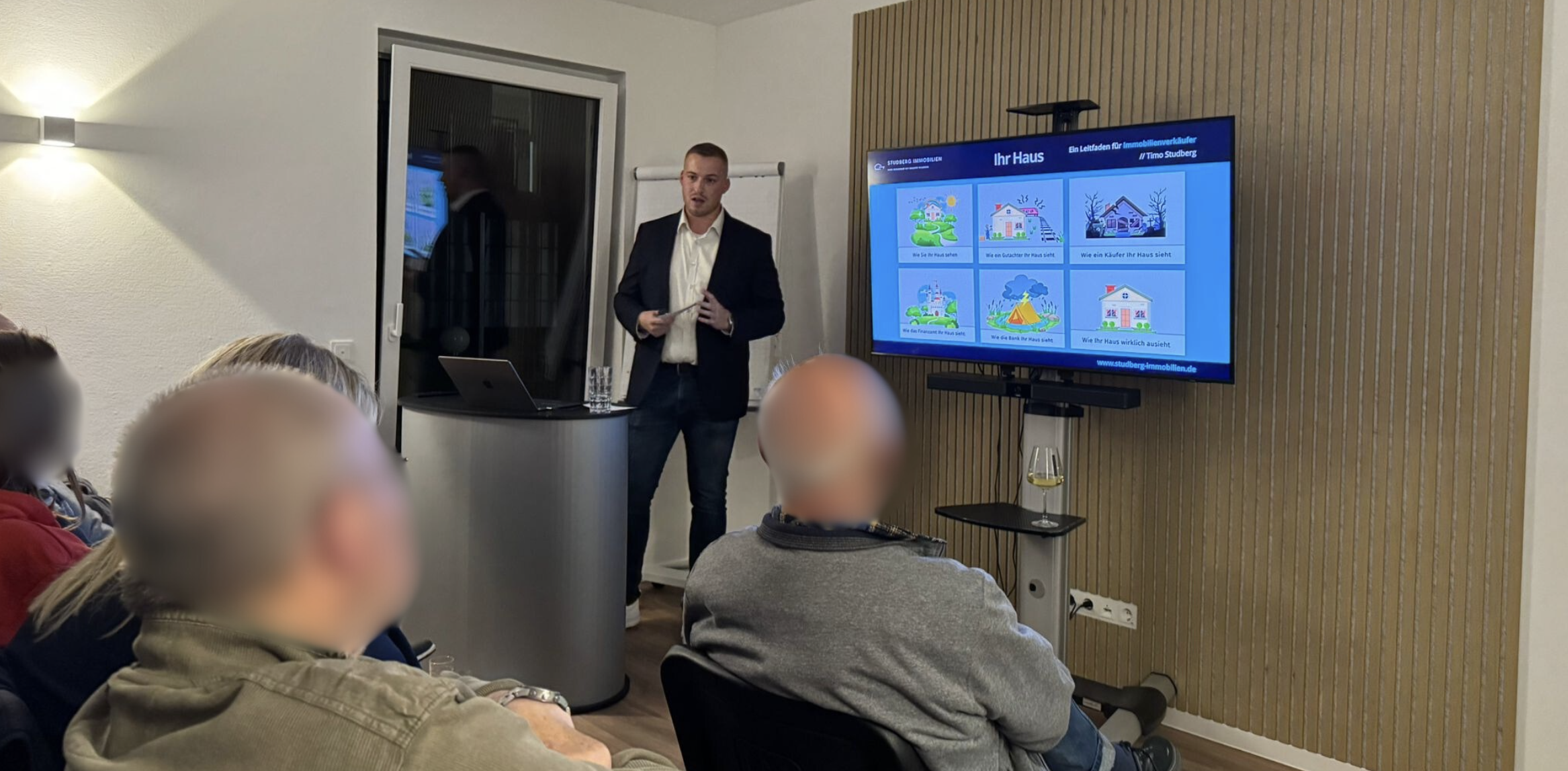 Vortrag von Studberg Immobilien vor Publikum in einem modern eingerichteten Raum mit Präsentation auf einem Bildschirm.