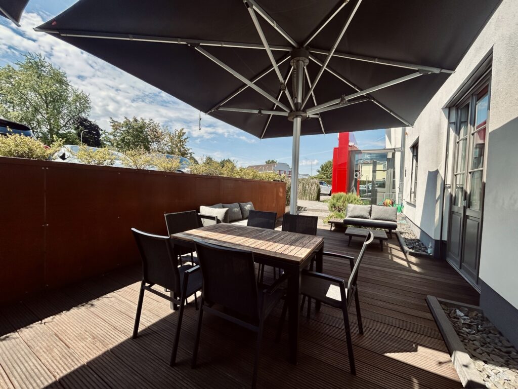 Terrasse des Denkwerks Herford mit großem Sonnenschirm, Sitzgruppe und Lounge-Möbeln – ein stilvoller Außenbereich für Pausen, Meetings und Networking.