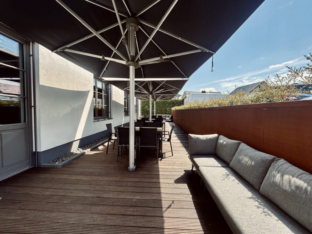Sonnige Außenterrasse des Denkwerks Herford mit großzügigen Sonnenschirmen, Sitzgruppen und Lounge-Sofa – ideal für Pausen, Networking und Business-Events im Freien.