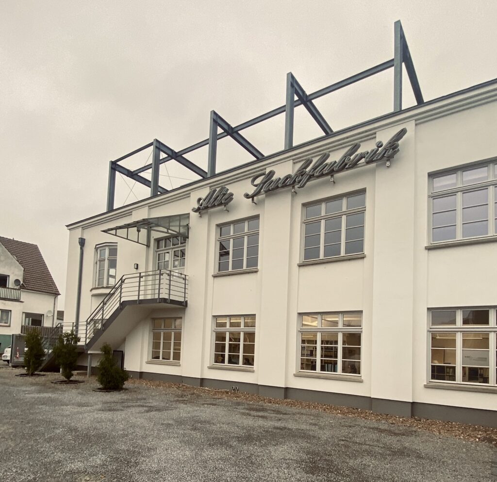 Außenansicht des Denkwerk Herford in der ehemaligen Alten Zuckerfabrik mit markanter Industriearchitektur, historischem Schriftzug und modernem Eingangsbereich.