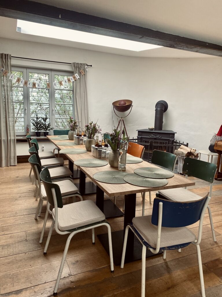Gemütlicher Veranstaltungsraum in der Sackfabrik Herford mit großer Tafel, stilvoller Dekoration, Kaminofen und wohnlichem Ambiente für Meetings, Workshops und private Feiern.