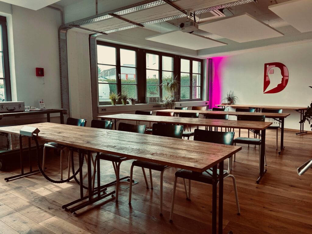 Seminarraum im Denkwerk Herford mit U- bzw. Klassenbestuhlung, Holztischen, moderner Präsentationstechnik und heller Industriearchitektur für Workshops und Schulungen.