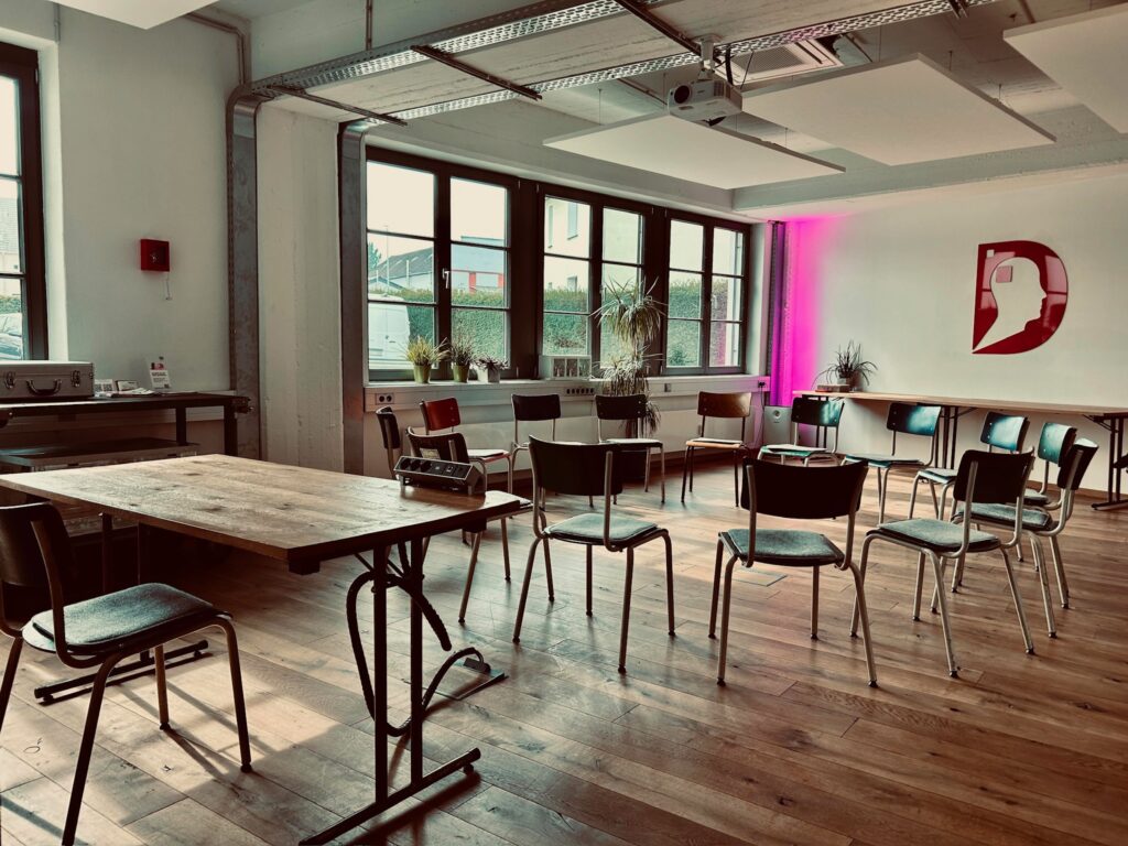 Workshopraum im Denkwerk Herford mit Stuhlkreis, Moderationstisch, großen Fensterfronten und moderner Präsentationstechnik – ideal für Workshops, Coachings und interaktive Seminare.
